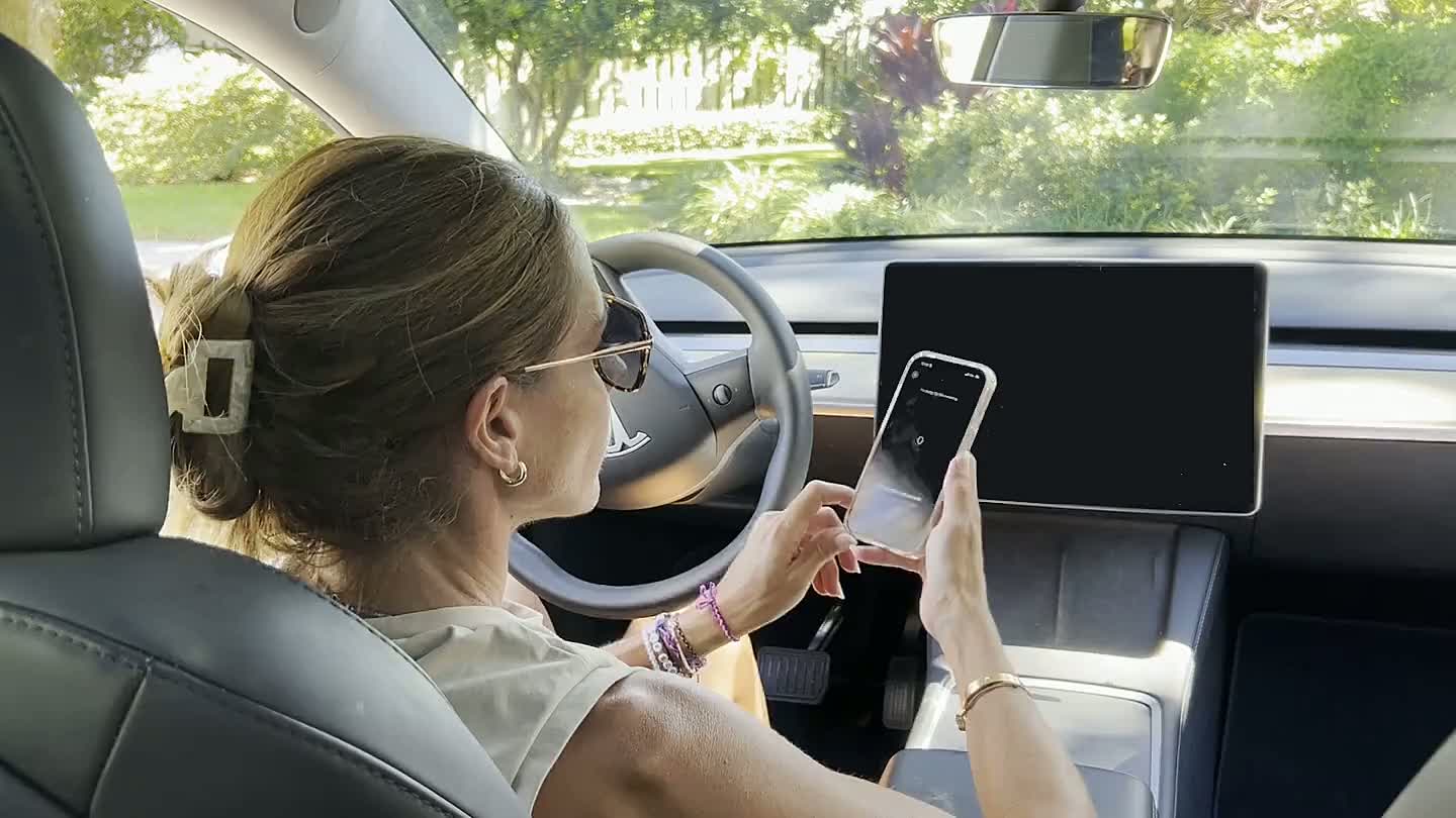 A woman doing a SomaCheck phone gesture in a parked car